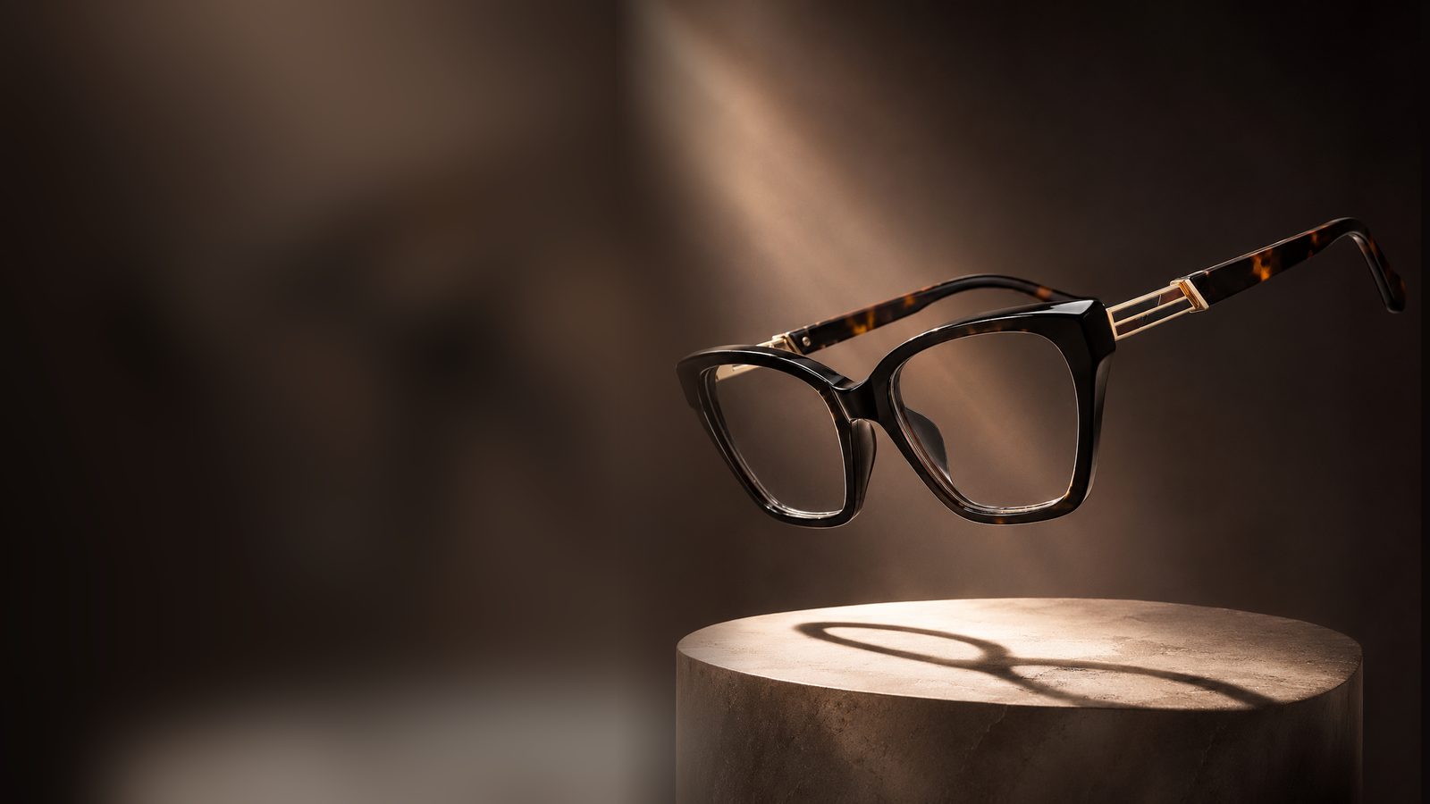 A tortoiseshell cat-eye eyeglass frame floating above a stone pedestal in warm light